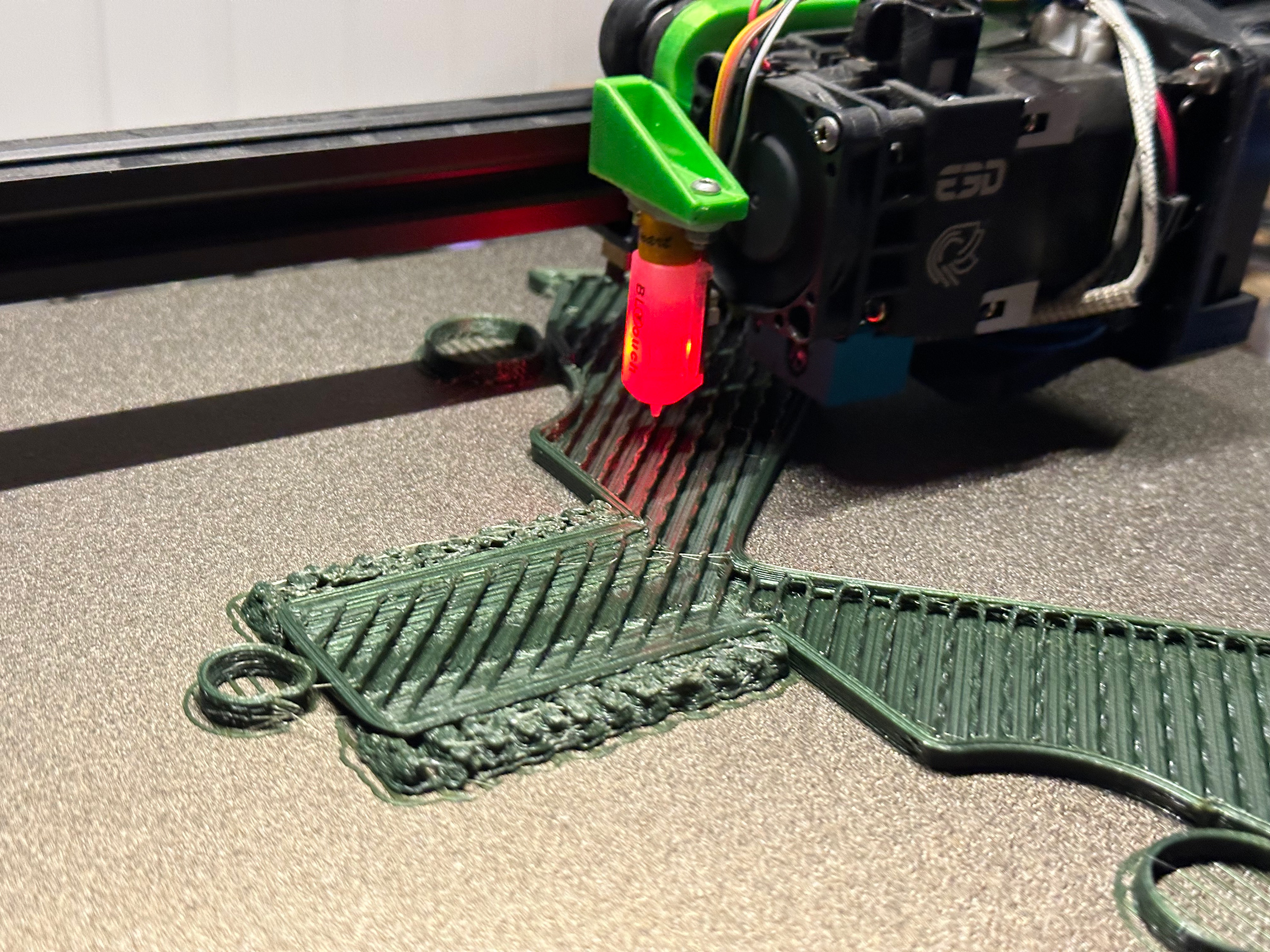 3D printer extruding green plastic on a gold build plate