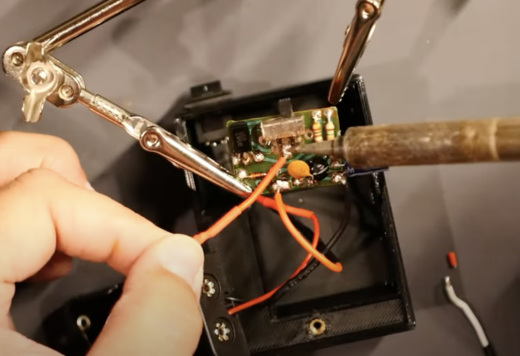 hand holding wires in place as they're soldered to a circuit board