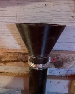 Black funnel installed in 3" drainage pipe on blue-gray wall