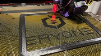 3d printer with custom hotend shroud printing a first layer with black pla